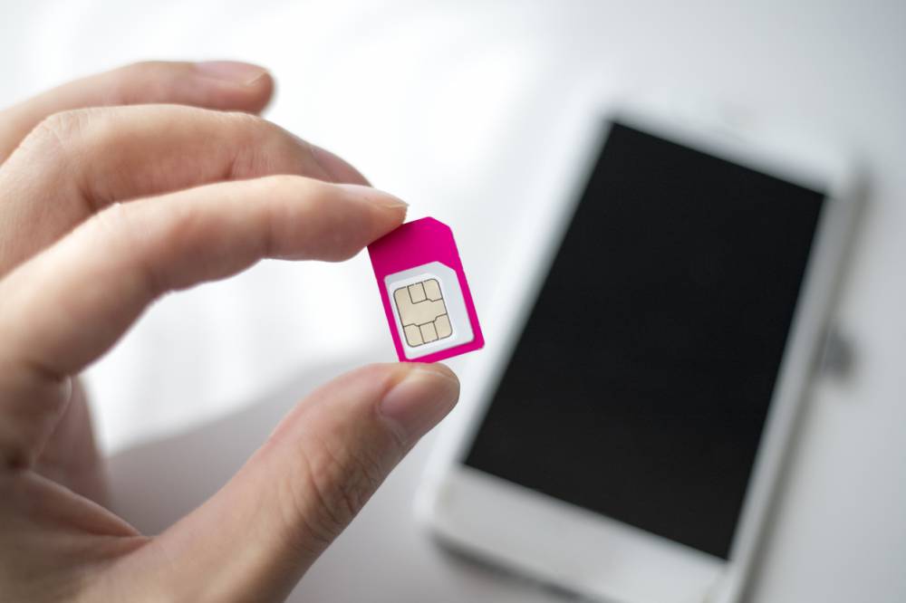 Carte SIM tenue entre le pouce et l'index devant un smartphone